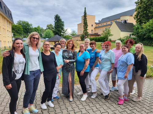 Eine Gruppe lachender Frauen, darunter eine Andrea Berg-Doppelgängerin, steht vor einem Gebäude.